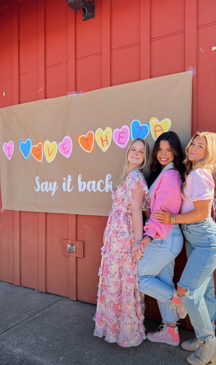 three girls standing in front of a sign that says say it back with hearts on it