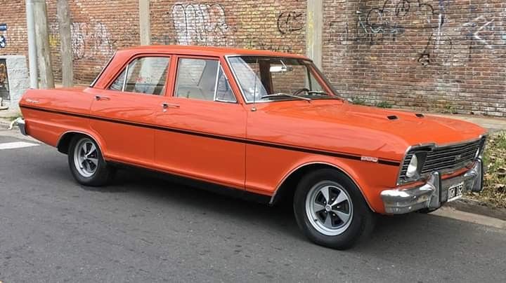 an orange car is parked on the side of the road in front of a brick wall