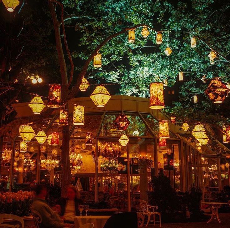 many lanterns are lit up in the night sky above a restaurant with tables and chairs