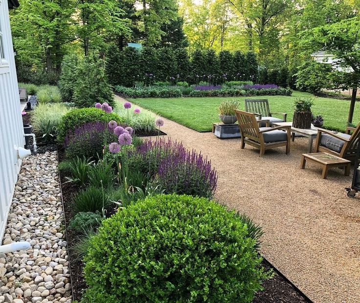 an outdoor patio with chairs and gravel path leading to the back yard, surrounded by greenery