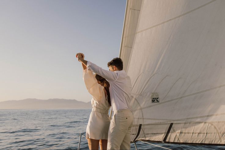 a man and woman standing on the deck of a sailboat