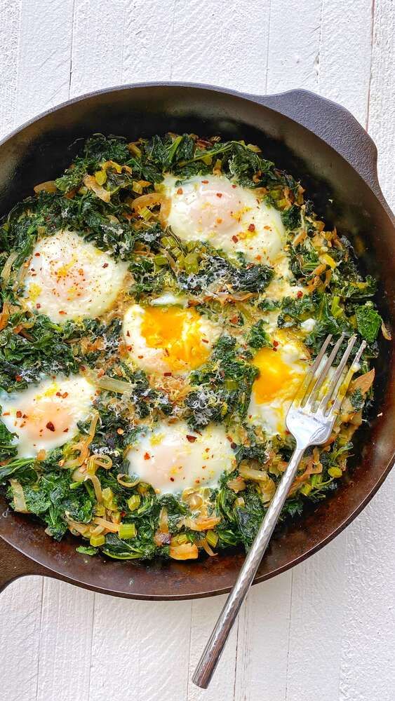 an iron skillet with eggs and spinach on it next to a knife and fork