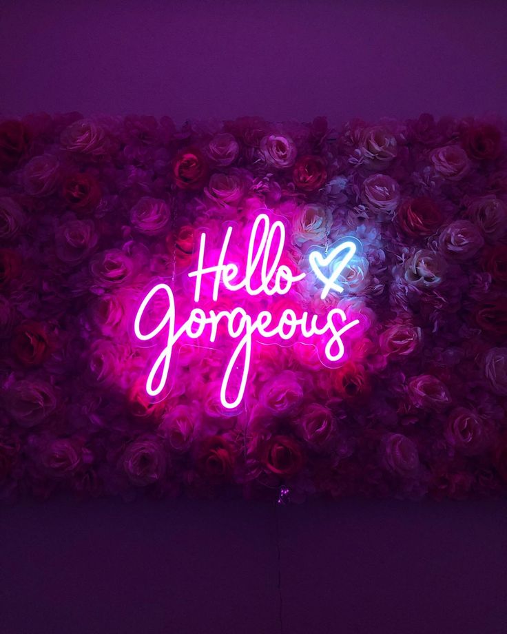 a neon sign that says hello gorgeous in front of some pink and purple roses on the wall