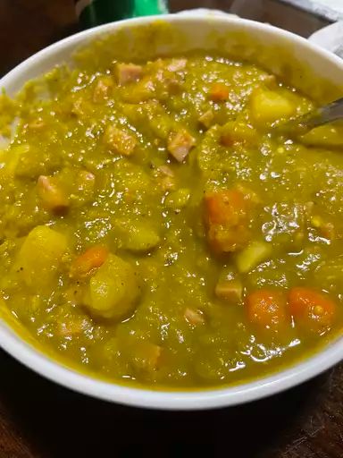 a white bowl filled with soup sitting on top of a wooden table next to a green cup