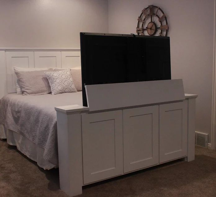 a bed with a tv on top of it next to a white dresser and door