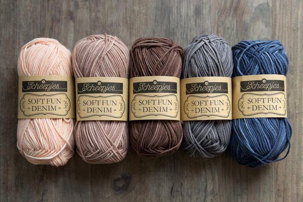 six skeins of soften denim yarn in various colors on a wooden surface