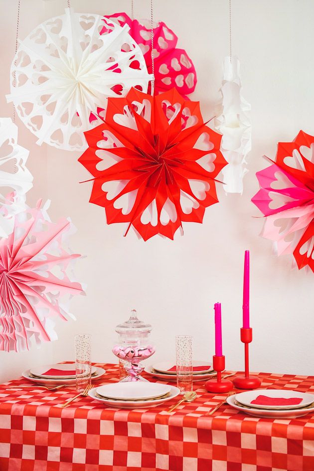 red and white paper umbrellas hanging from the ceiling above a table with place settings on it