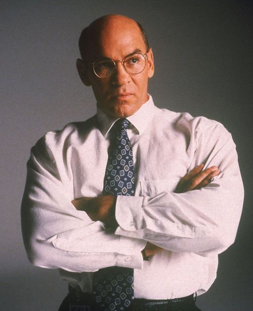 an older man wearing glasses and a white shirt is posing with his arms crossed in front of him