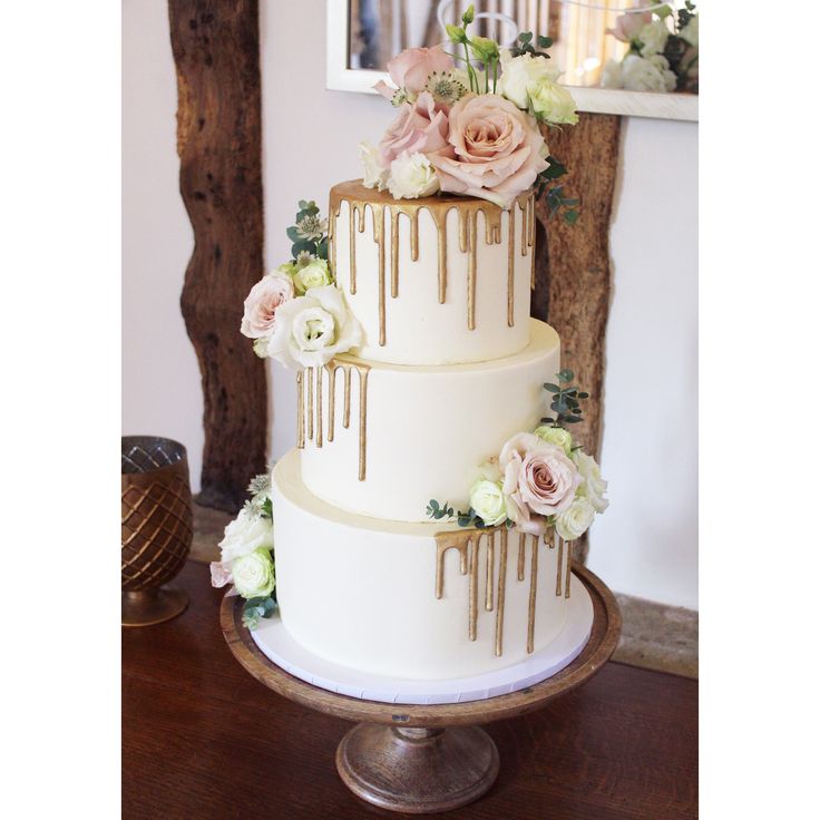 a three tiered wedding cake with flowers and dripping icing on the top layer