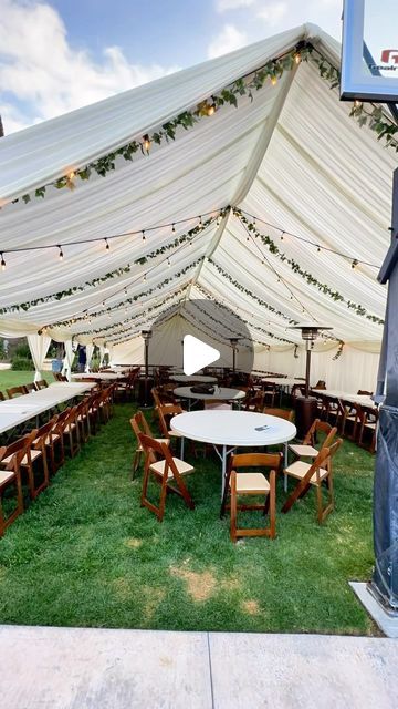 a large white tent with tables and chairs in the grass under lights on an outdoor basketball court