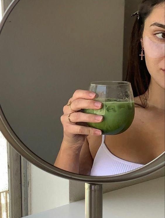 a woman holding a green drink in front of a mirror