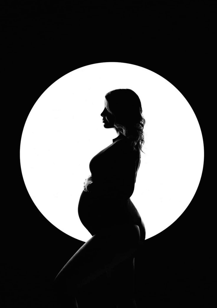 a pregnant woman standing in front of a full moon