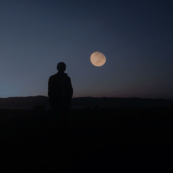 a man standing on top of a hill under a full moon