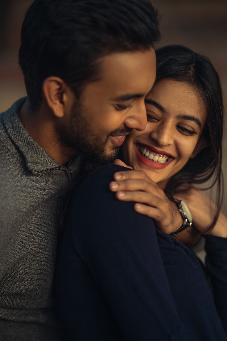 a man and woman embracing each other with their arms around one another while smiling at the camera