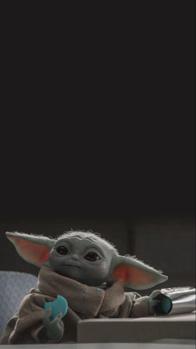 a baby yoda is sitting on a table with a remote control in it's hand