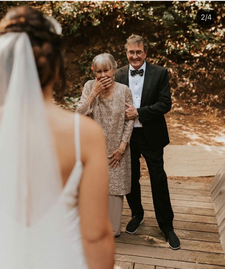 a man and woman standing on a wooden walkway next to each other, with trees in the background