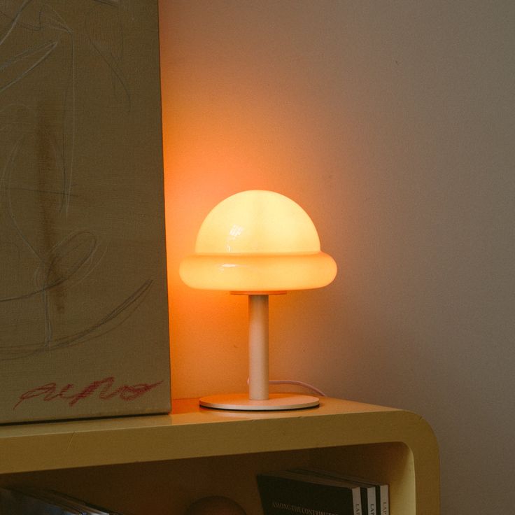 a lamp sitting on top of a wooden shelf next to a book case and a painting