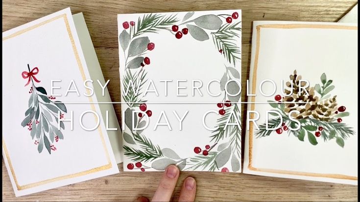 two cards with holly and pine cones on them, one is being held up by someone's hand