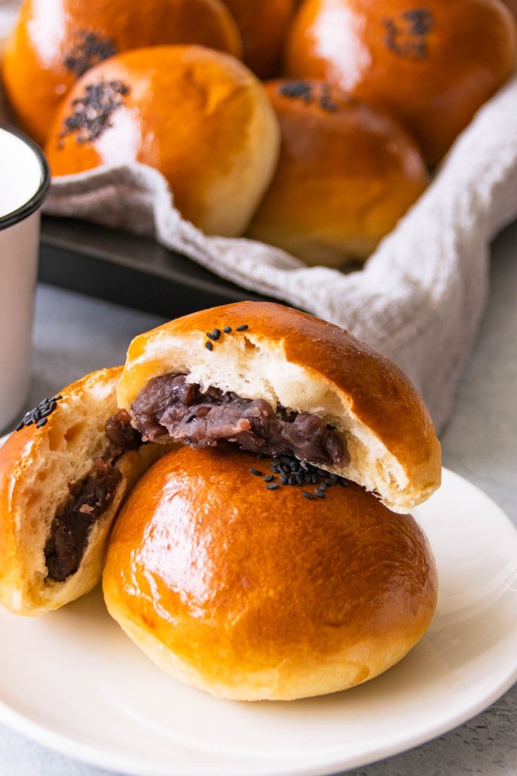 two rolls on a plate next to a cup of coffee and muffins in the background