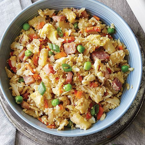 a bowl filled with rice, peas and ham on top of a table next to a fork