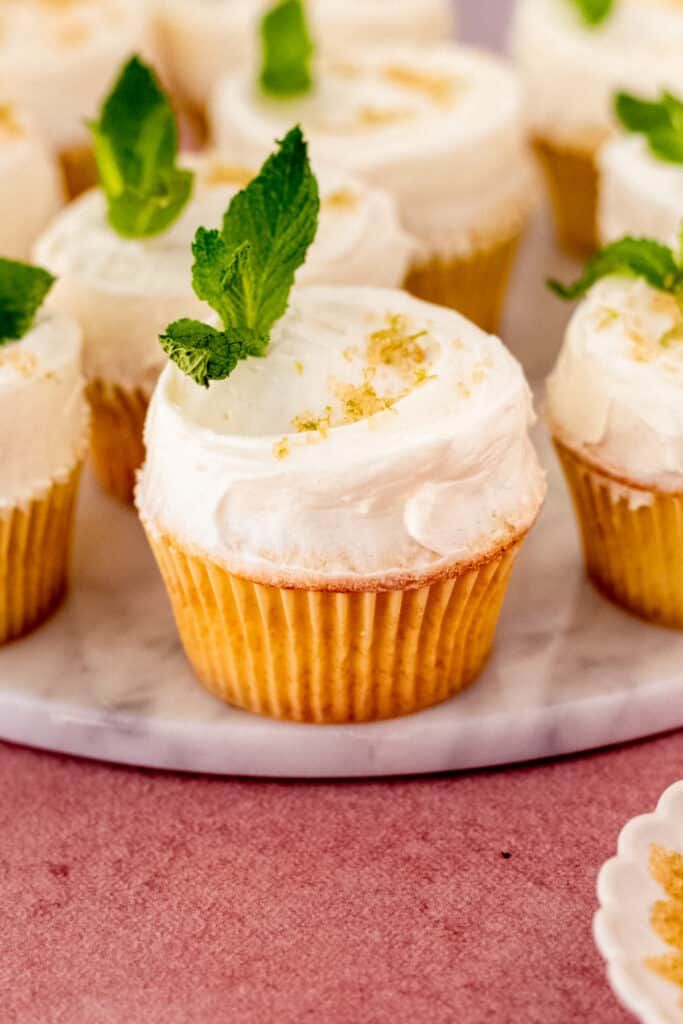 small cupcakes with white frosting and green leaves on them sitting on a plate