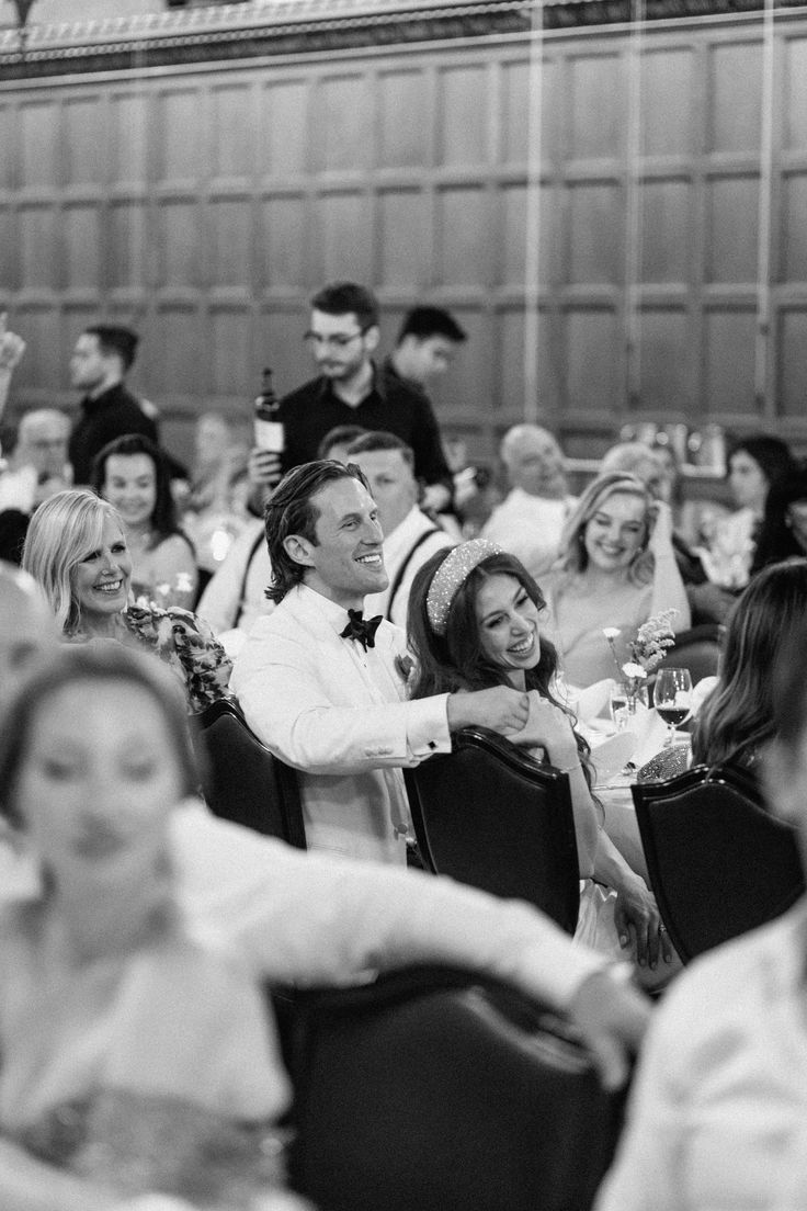 a black and white photo of people sitting at tables in a banquet hall with wine glasses on the table