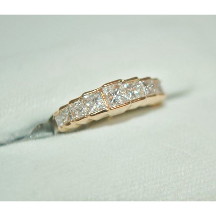 a wedding ring with three princess cut diamonds on it's side, sitting on a white cloth