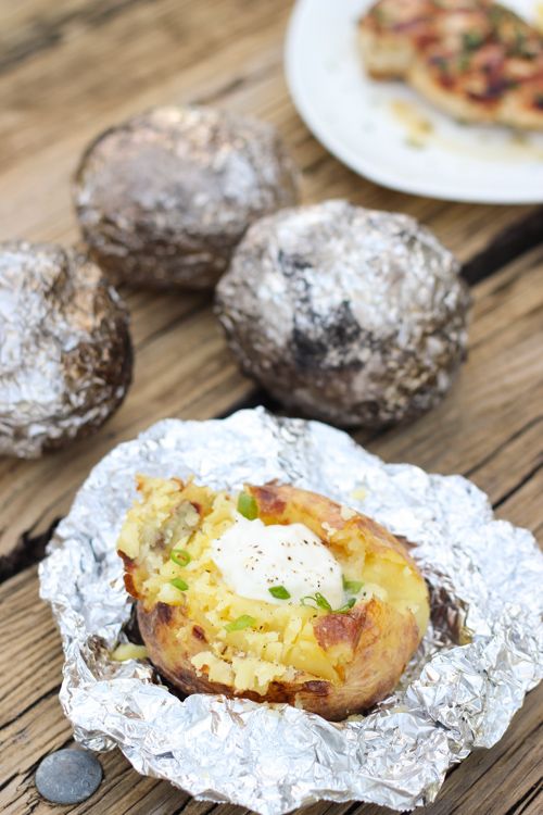 some food is sitting on tin foil on a wooden table with other foods in the background