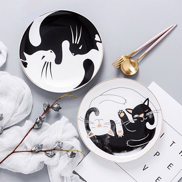 two black and white plates with cats painted on them next to napkins, forks and spoons