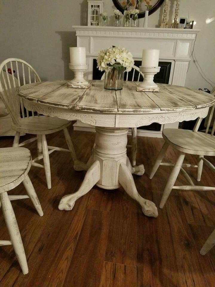 a white table with four chairs around it and a vase filled with flowers on top