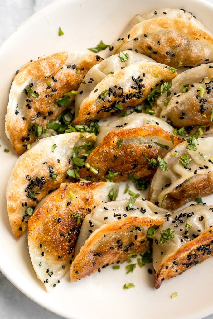 a white bowl filled with dumplings covered in sauce and seasoning sprinkles