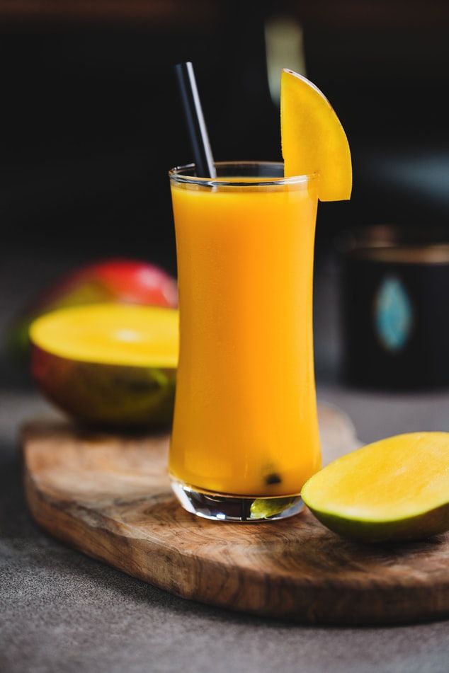 a glass filled with orange juice next to slices of fruit on a wooden cutting board