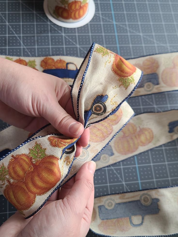 someone is sewing fabric on the edge of a piece of cloth with pumpkins printed on it