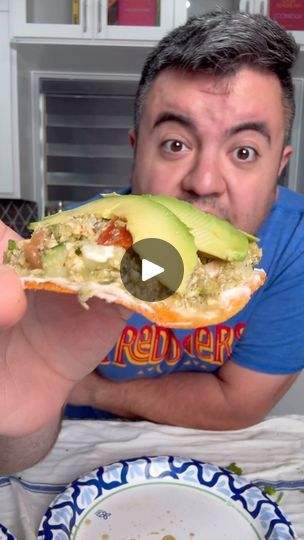 the man is eating an avocado sandwich with his mouth wide open and holding it in one hand