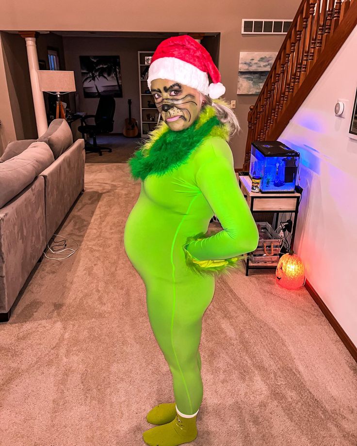 a woman dressed in green and wearing a santa claus hat is standing in the living room