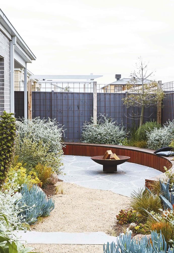 a circular bench sits in the middle of a garden with succulents and trees