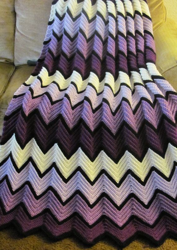 a purple and white crocheted blanket sitting on top of a couch next to a pillow