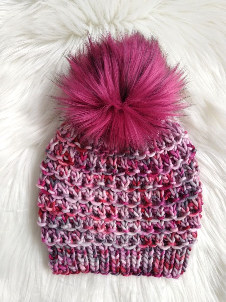 a pink and purple knitted hat with a pom - pom on top