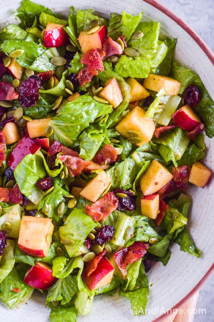 a salad with lettuce, apples and cranberries in a white bowl