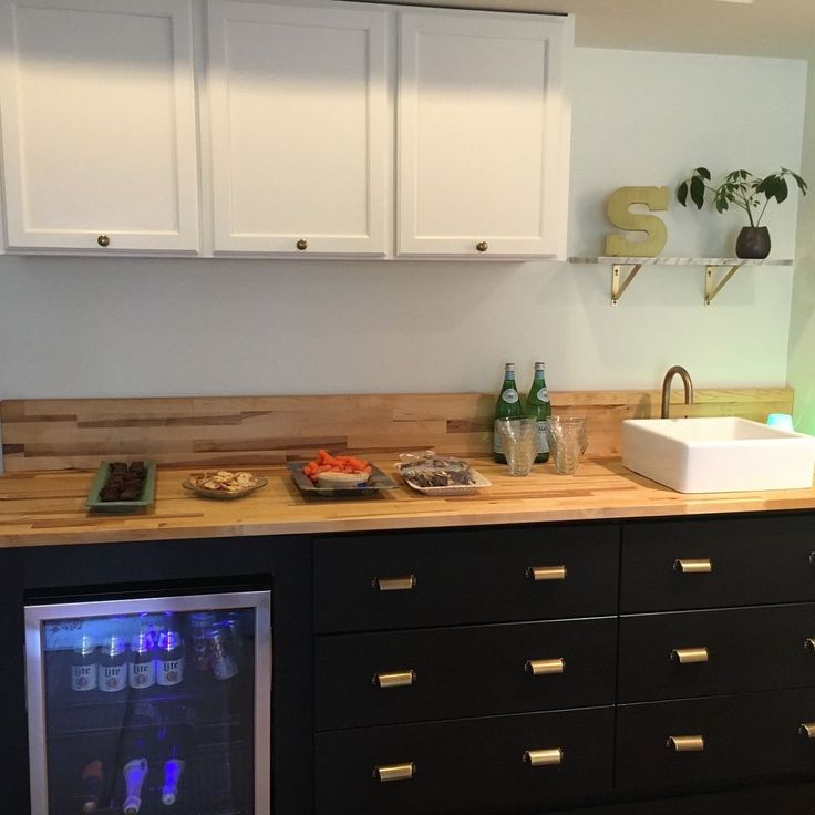 a kitchen with white cupboards and black drawers has a wine cooler on the counter