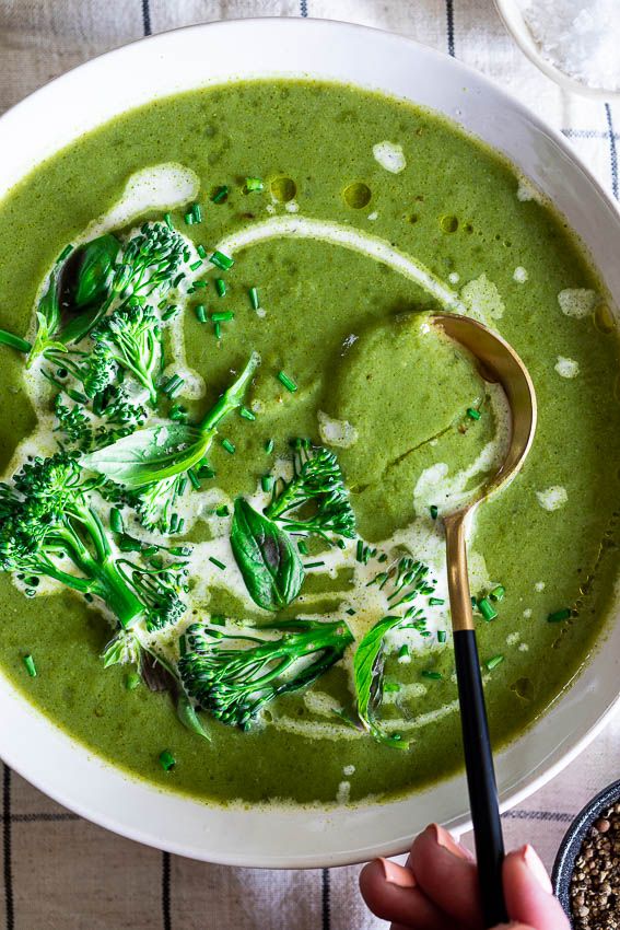 a white bowl filled with broccoli soup on top of a table next to a spoon