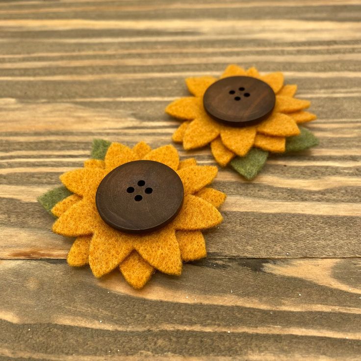 two brown and yellow flower shaped buttons sitting on top of a wooden table next to each other