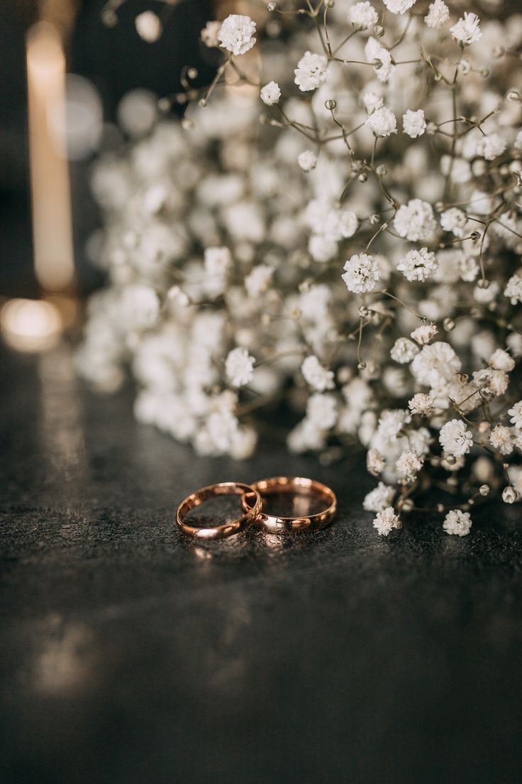 two gold wedding rings sitting on top of a table next to white flowers and candles