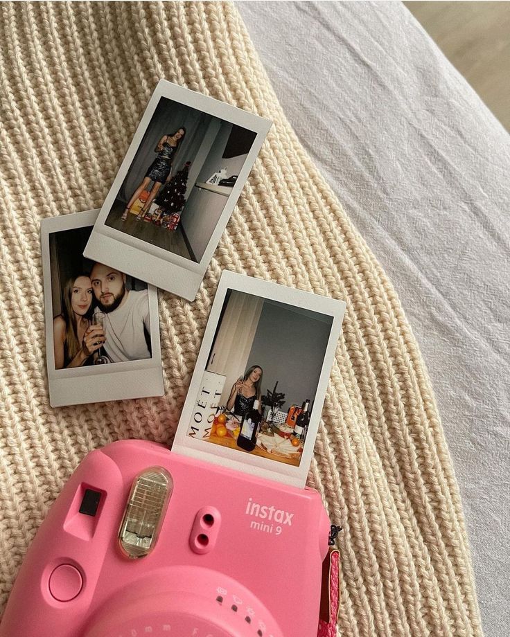 an instax camera sitting on top of a bed next to two pictures and a pink polaroid