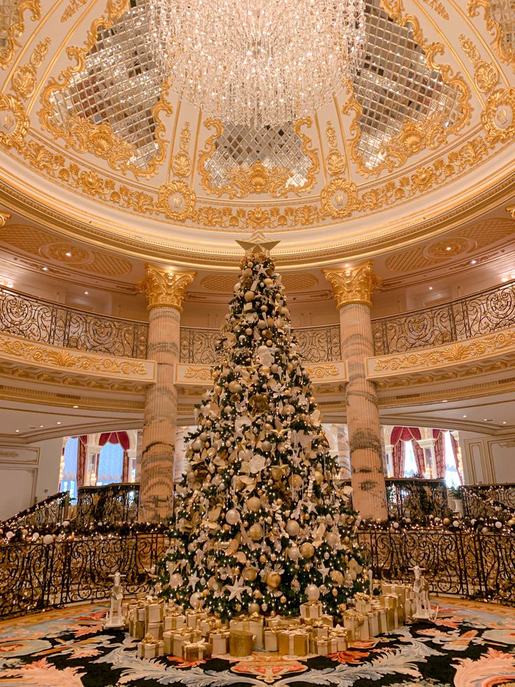 a large christmas tree in the middle of a room with chandelier and stairs