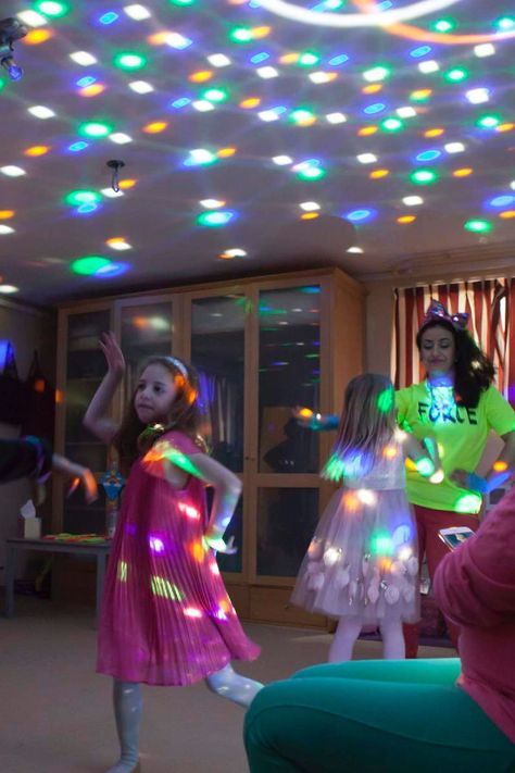 children are dancing in the living room with colorful lights on the ceiling