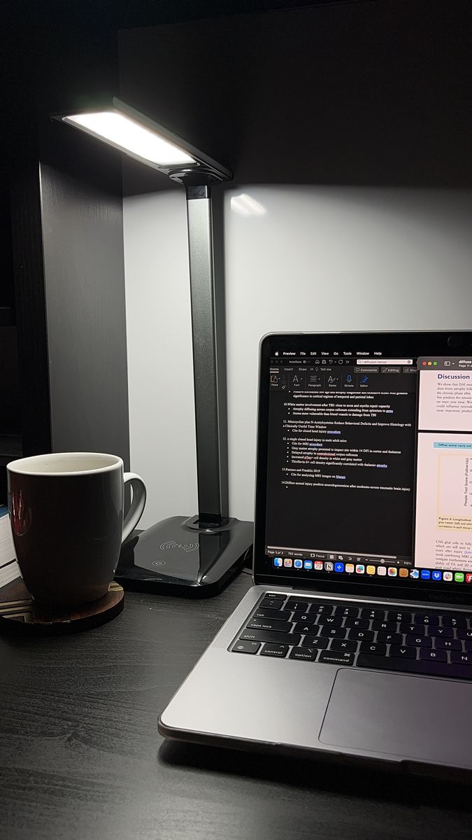 an open laptop computer sitting on top of a desk next to a coffee cup and lamp