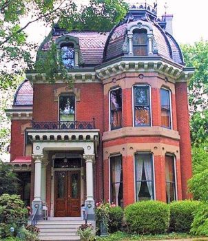 a large red brick house sitting in the middle of a lush green yard