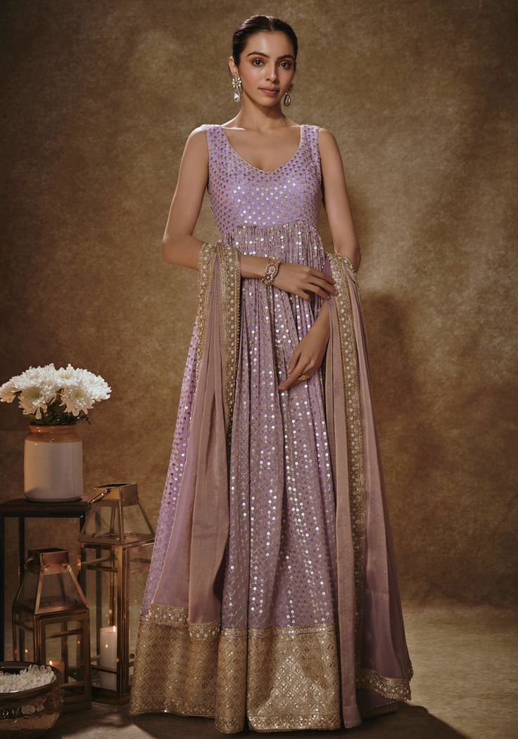 Step into a world of elegance and grace with our Lilac And Gold Embroidered Anarkali Set. Crafted in soft georgette, this enchanting lilac gown is adorned with delicate thread and sequins embroidery, adding a touch of sparkle to your look. The curved V-neckline adds a flattering touch, while the shimmering tissue dupatta completes the ensemble with boota, dori, cutdana, and pearl detailing. Perfect for mehendi ceremonies or as a wedding guest, this set exudes charm and sophistication. Embrace the beauty of tradition with this stunning Anarkali set. Composition : Anarkali - Viscose georgette, Dupatta - Shimmer Tissue Care: Dry Clean Only and Vacuum Storage This product can be customized for sleeves, length of blouse and neckline Delivery : 4-6 weeks as the product is hand crafted. Check Siz Anarkali For Wedding Guest, Anarkali Sequin Gown For Diwali, Diwali Anarkali Gown With Sequins, Floor-length Anarkali Set With Sequins, Anarkali Lavender Sharara With Resham Embroidery, Anarkali Lavender Sharara For Reception, Bollywood Lavender Anarkali Set With Resham Embroidery, Floor-length Sequined Anarkali Set For Eid, Anarkali Sequin Gown For Eid