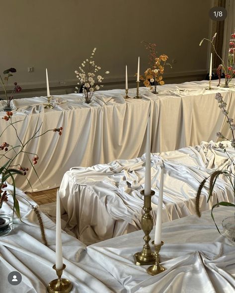 several candles are lined up on the table covered with white cloths and flower arrangements